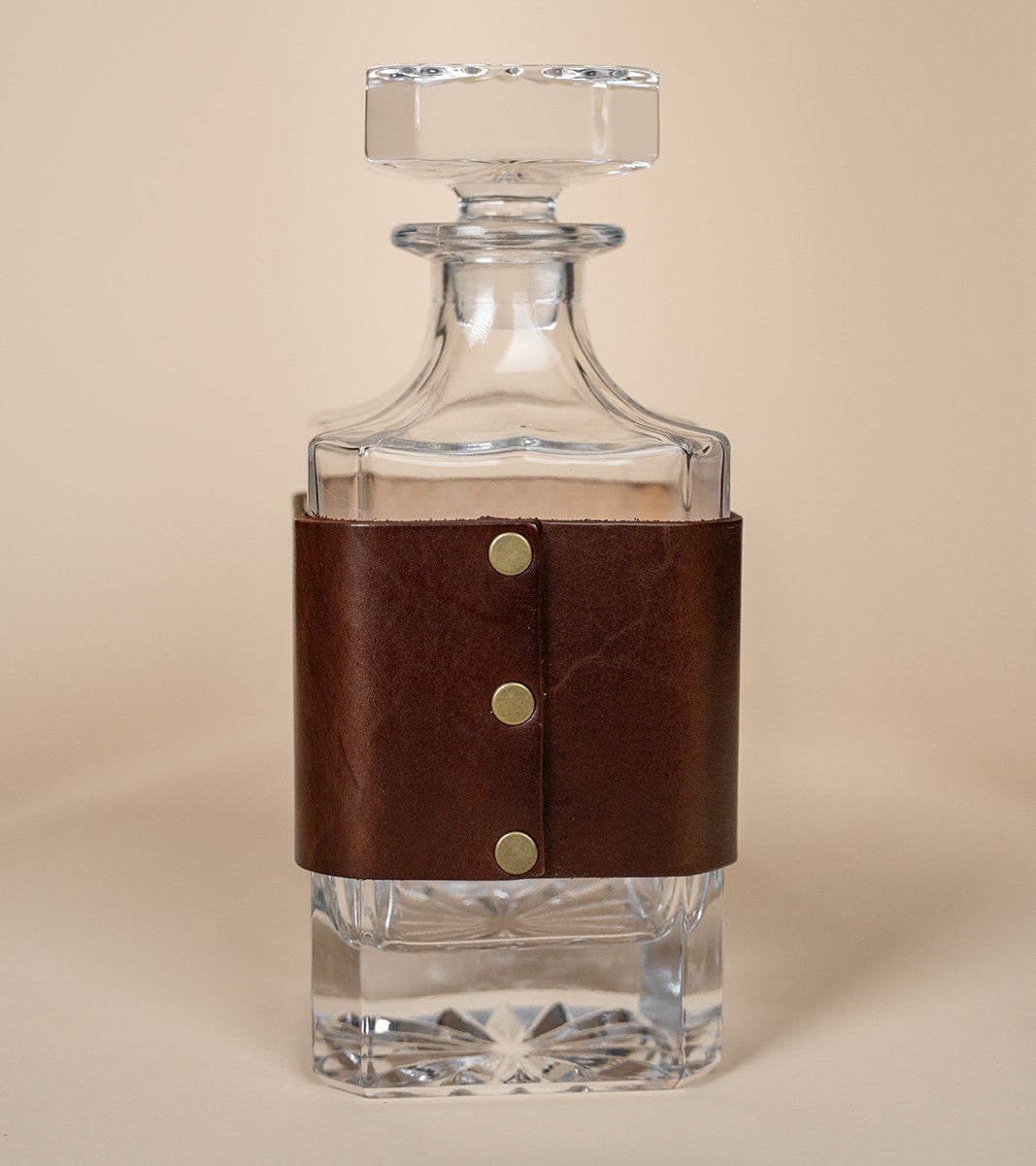 Clear glass decanter with a brown leather wrap on a beige background