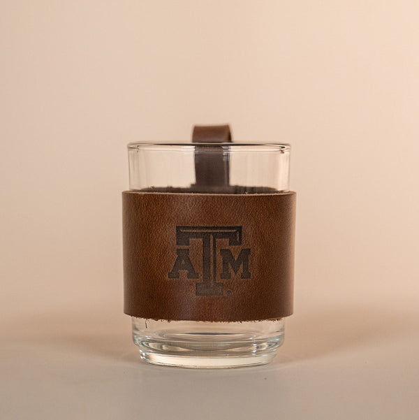 Clear glass with a brown leather sleeve featuring a Texas A&M stamped debossed logo on a beige background