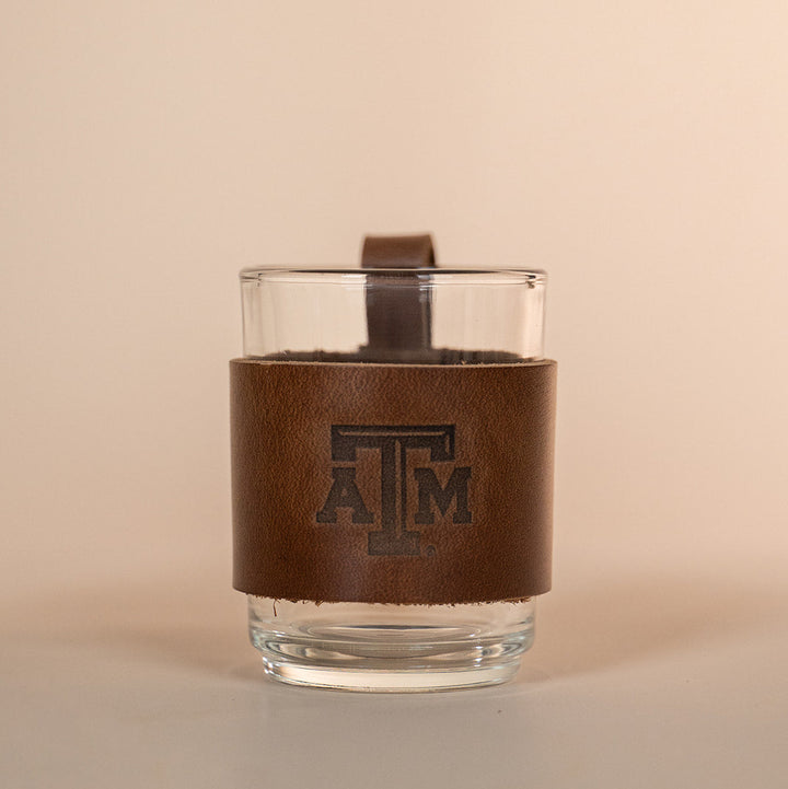Clear glass with a brown leather sleeve featuring a Texas A&amp;M stamped debossed logo on a beige background
