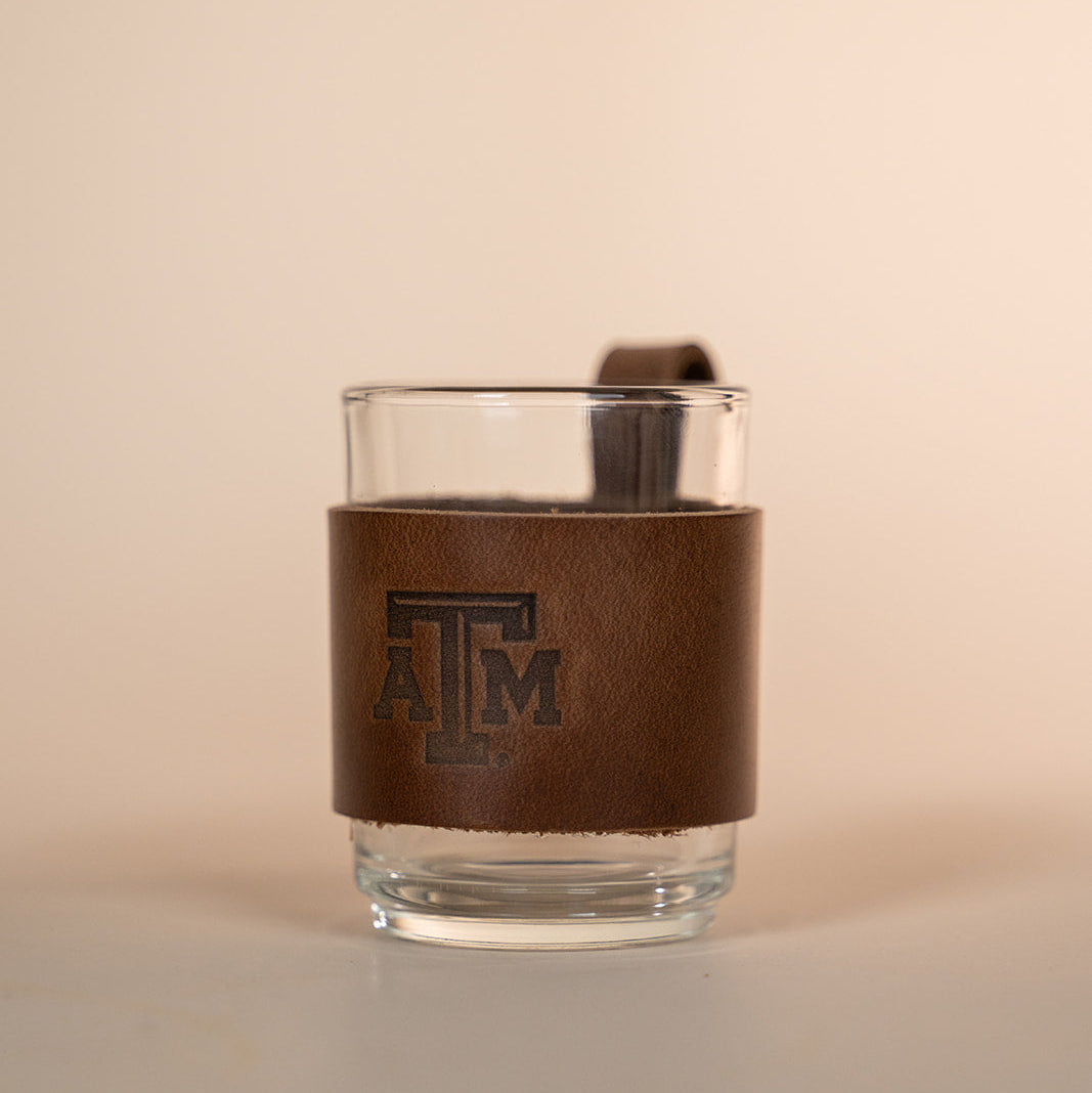 Clear glass with a brown leather sleeve featuring a Texas A&amp;M stamped debossed logo on a beige background