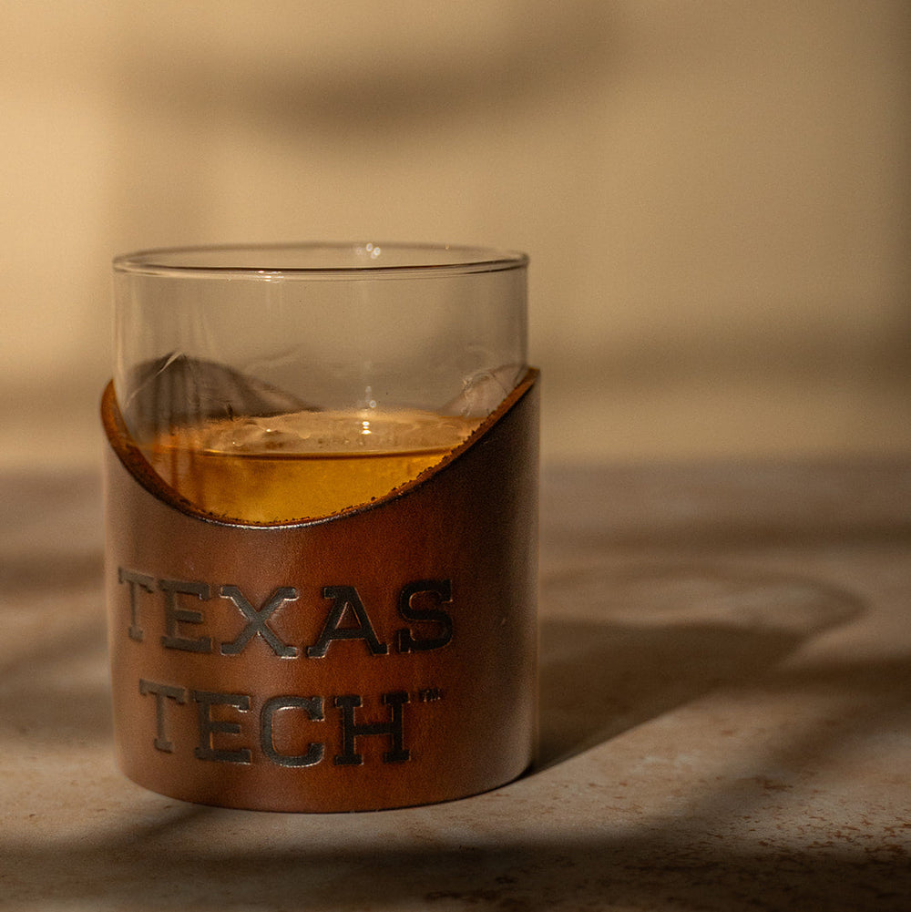 Rocks glass with a premium leather wrap displaying 'Texas Tech' on a textured surface.