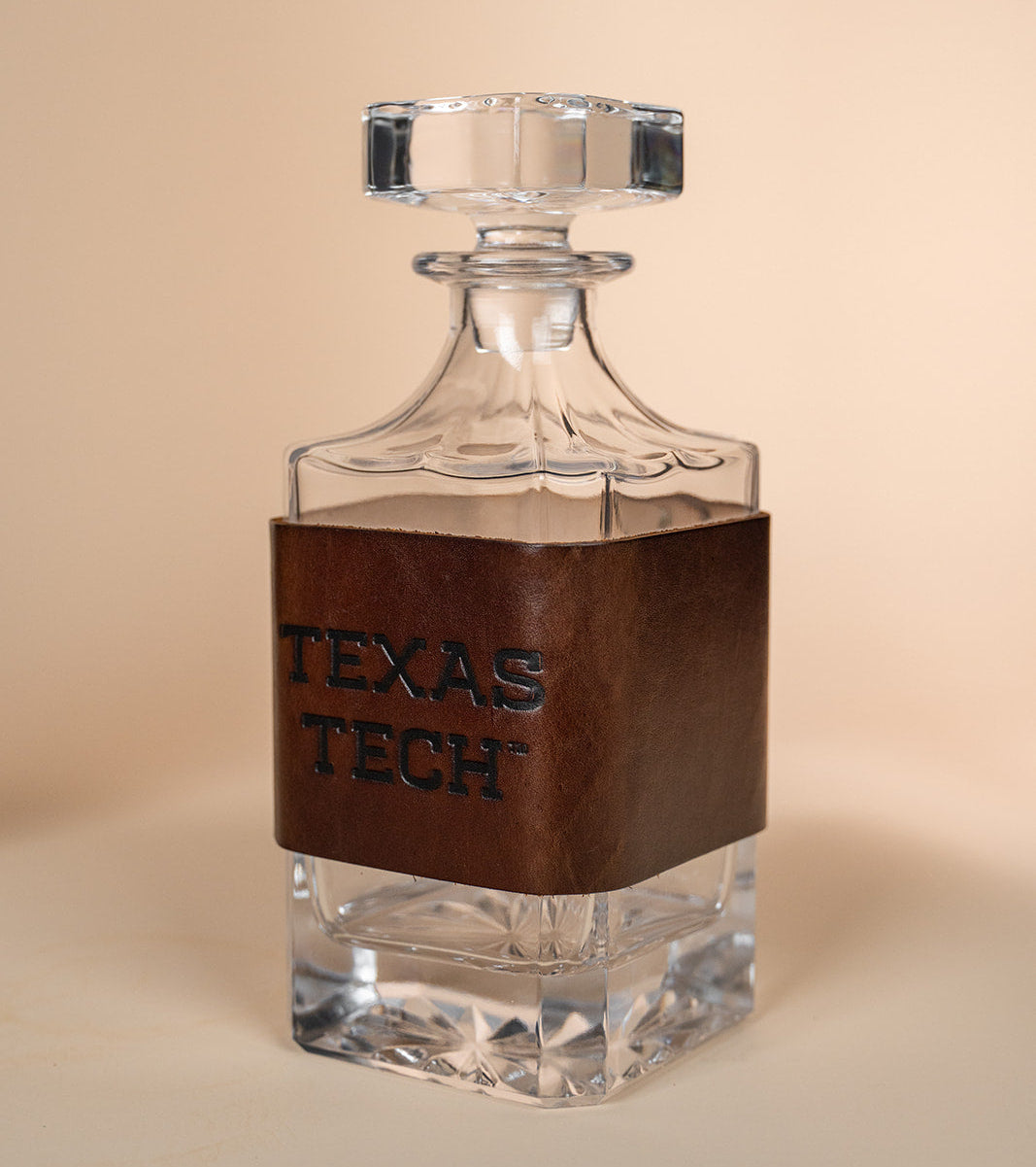Clear glass decanter with brown leather wrap displaying &
