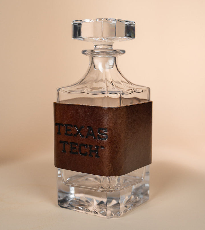 Clear glass decanter with brown leather wrap displaying &