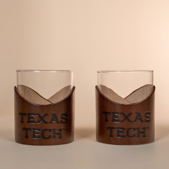 Two lowball rocks glasses with brown leather sleeves displaying &
