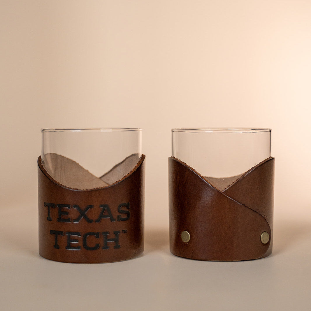 Two lowball rocks glasses with brown leather sleeves displaying &