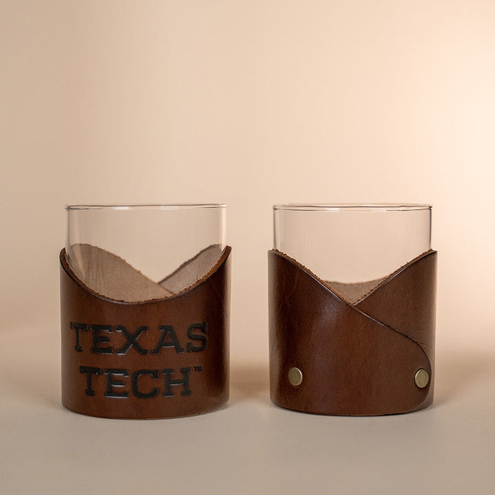 Two lowball rocks glasses with brown leather sleeves displaying &